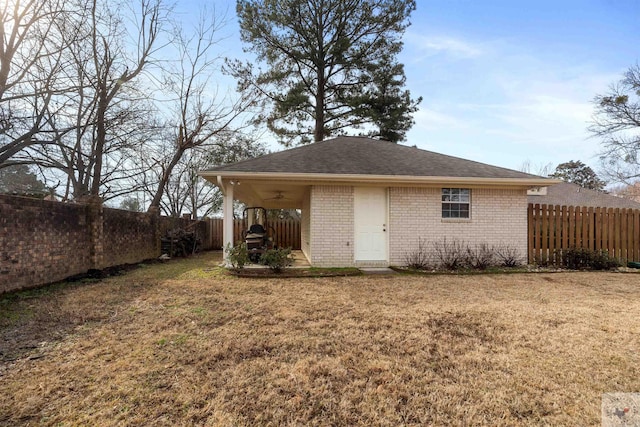 back of property featuring a yard, a fenced backyard, roof with shingles, and brick siding