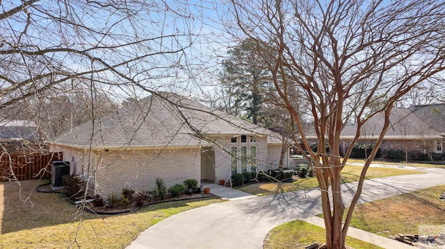 view of front of home with brick siding, a front yard, and central air condition unit