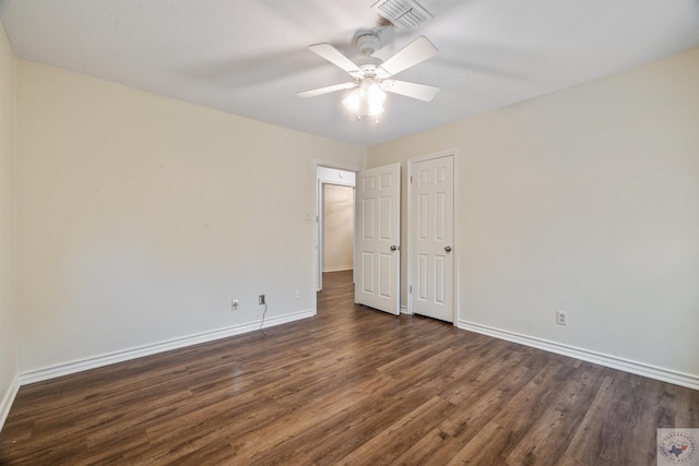 empty room with dark wood-style floors, visible vents, baseboards, and a ceiling fan