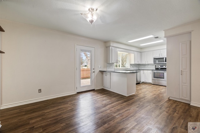 kitchen with a peninsula, white cabinetry, appliances with stainless steel finishes, decorative backsplash, and dark countertops