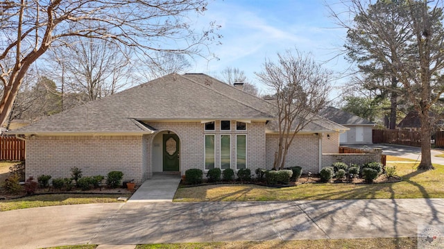 view of front facade featuring a shingled roof, a front yard, and brick siding