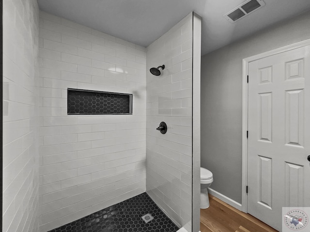 bathroom featuring wood-type flooring, toilet, and tiled shower