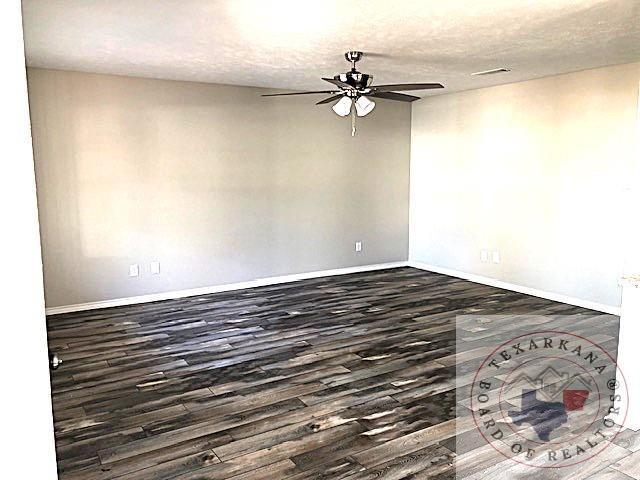 empty room featuring ceiling fan, a textured ceiling, dark wood-style flooring, visible vents, and baseboards