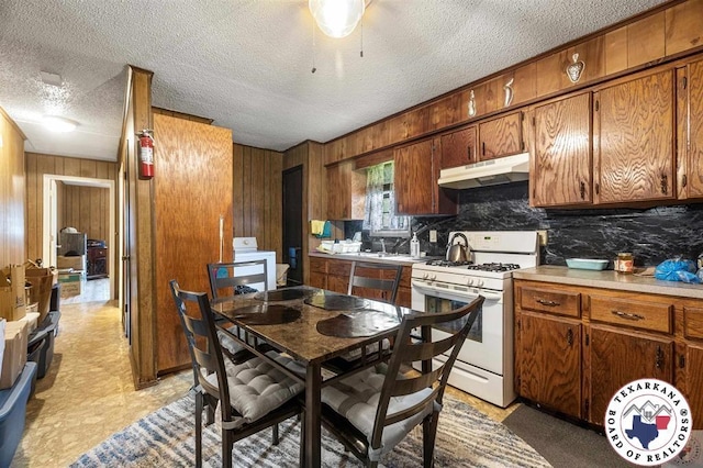 203 Pleasant Vly, Texarkana, AR 71854 - kitchen with white range with gas cooktop, under cabinet range hood, wood walls, brown cabinets, and light countertops