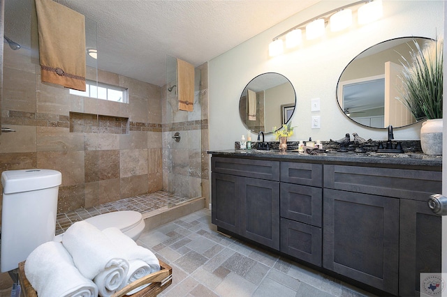 bathroom with a textured ceiling, toilet, vanity, and a tile shower