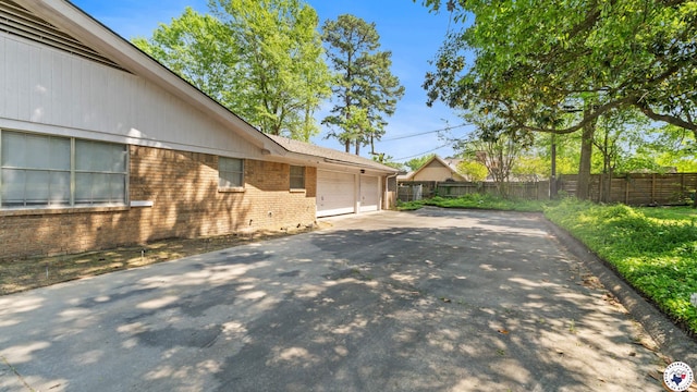 view of side of property with fence, aphalt driveway, brick siding, and a garage
