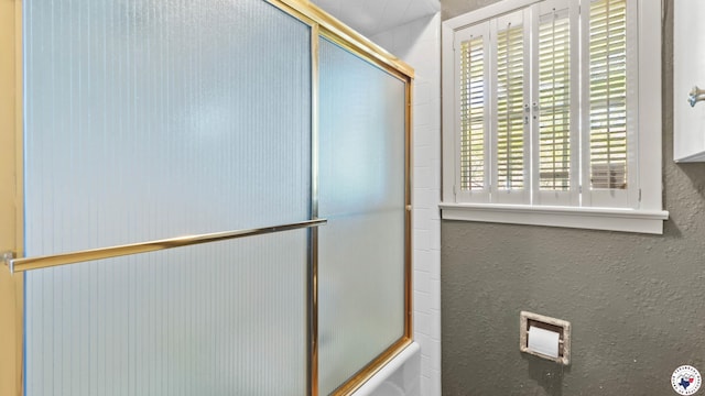 full bathroom featuring a textured wall and bath / shower combo with glass door