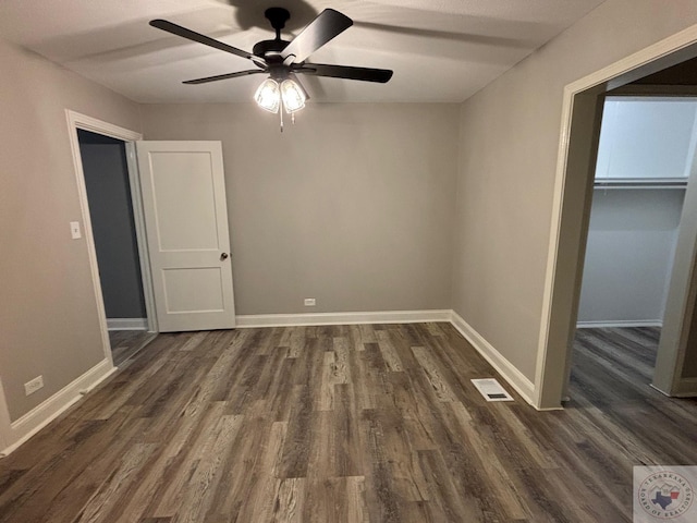 unfurnished bedroom featuring ceiling fan, dark wood-type flooring, a spacious closet, and a closet