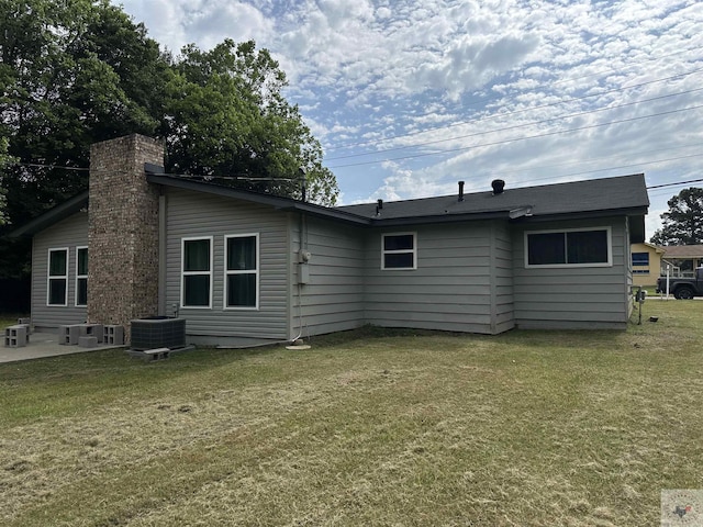 rear view of property with central air condition unit and a lawn