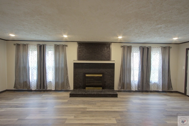 unfurnished living room with light hardwood / wood-style floors, a textured ceiling, and a brick fireplace