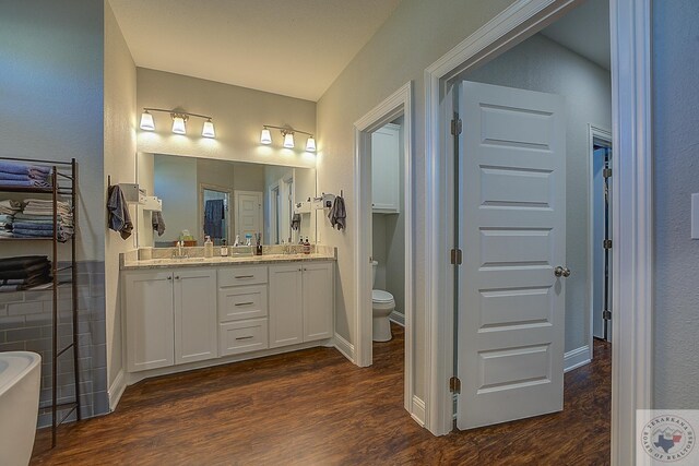 full bathroom with wood finished floors, double vanity, a freestanding bath, a sink, and toilet