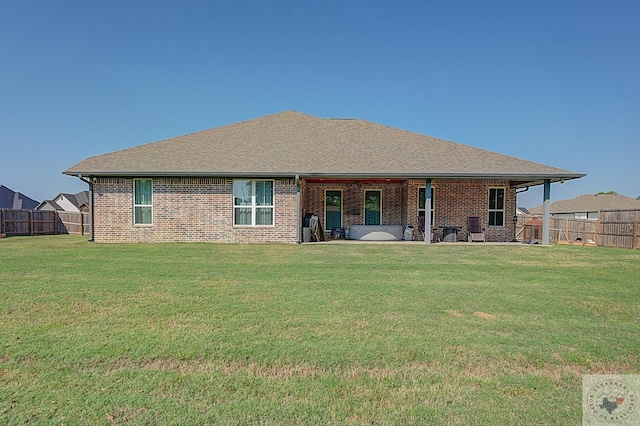 rear view of house with brick siding, a shingled roof, a yard, and fence