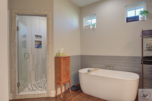 full bathroom with a shower stall, wainscoting, wood finished floors, a soaking tub, and tile walls