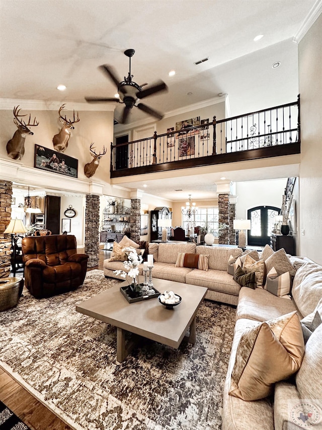 living room with ornate columns, crown molding, a fireplace, hardwood / wood-style floors, and ceiling fan with notable chandelier