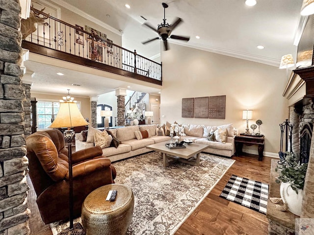 living room with a stone fireplace, decorative columns, hardwood / wood-style flooring, ornamental molding, and ceiling fan with notable chandelier