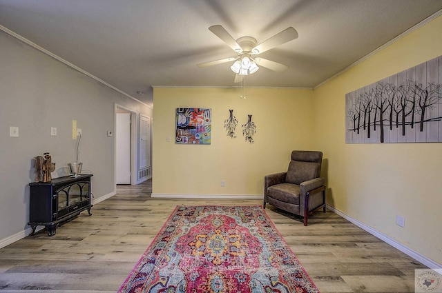 living area featuring ceiling fan, wood finished floors, ornamental molding, and a wood stove