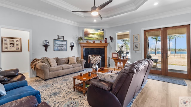 living area with light wood-type flooring, a fireplace, a raised ceiling, and crown molding