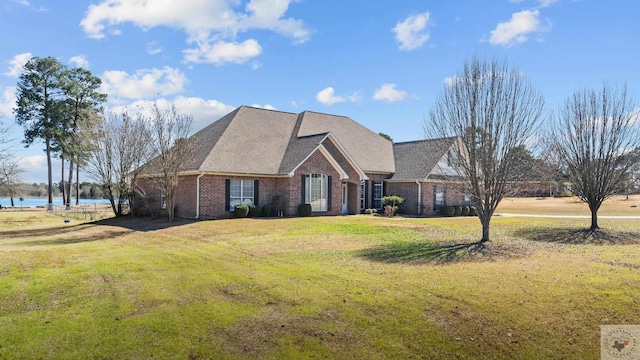 view of front of home featuring brick siding, a front lawn, a water view, and a shingled roof