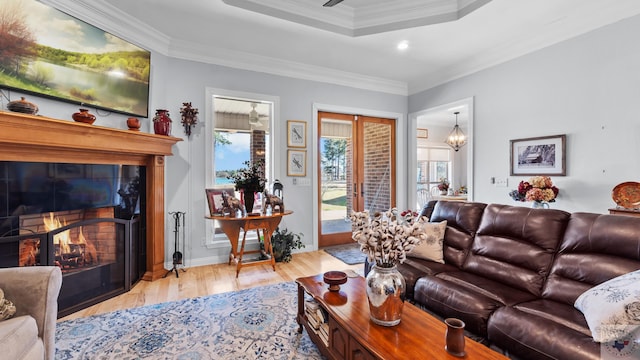 living room featuring a raised ceiling, ornamental molding, wood finished floors, a lit fireplace, and french doors