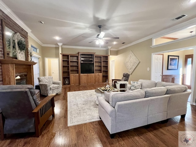 living room with a brick fireplace, visible vents, crown molding, and dark wood-style flooring