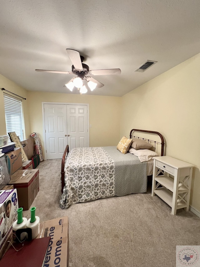 bedroom featuring a closet, light colored carpet, visible vents, a ceiling fan, and a textured ceiling