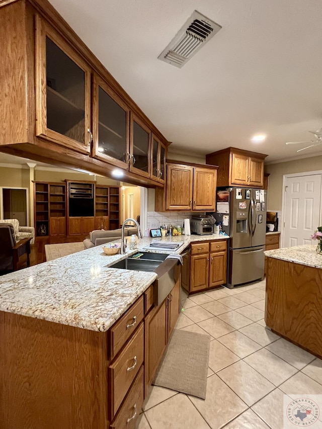 kitchen with a kitchen island with sink, visible vents, stainless steel fridge with ice dispenser, brown cabinets, and glass insert cabinets