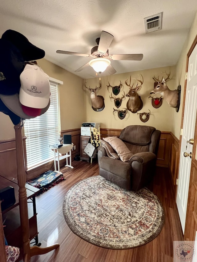 interior space featuring a wainscoted wall, dark wood-style floors, visible vents, and a ceiling fan