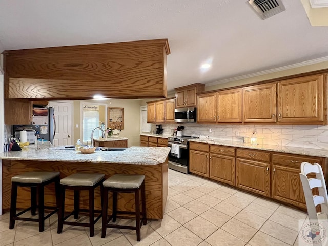 kitchen featuring visible vents, appliances with stainless steel finishes, decorative backsplash, brown cabinets, and light stone countertops