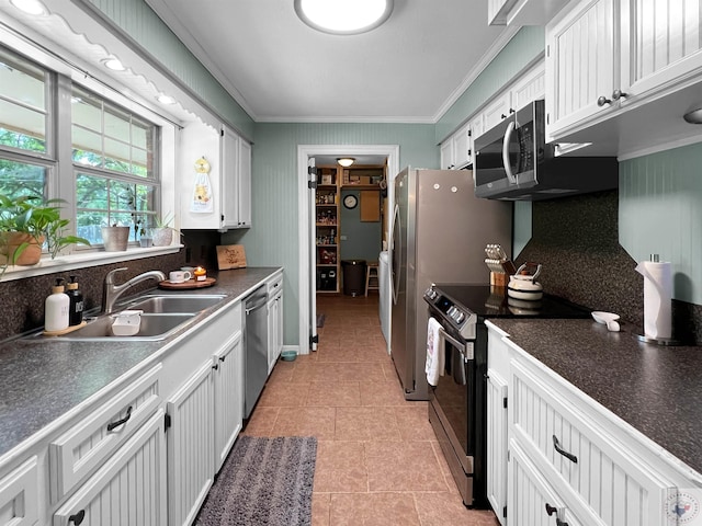 kitchen featuring appliances with stainless steel finishes, white cabinetry, sink, ornamental molding, and light tile patterned flooring