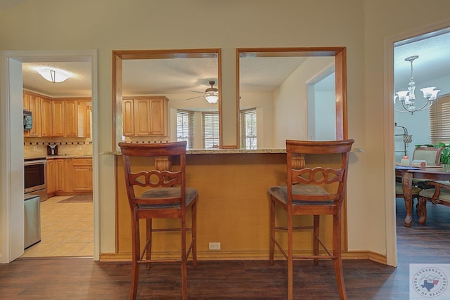 kitchen with light stone countertops, hardwood / wood-style floors, tasteful backsplash, a kitchen breakfast bar, and hanging light fixtures