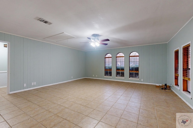 empty room with light tile patterned floors, a ceiling fan, baseboards, visible vents, and crown molding