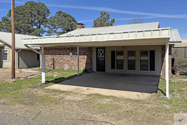 view of front of house with a chimney, metal roof, and brick siding