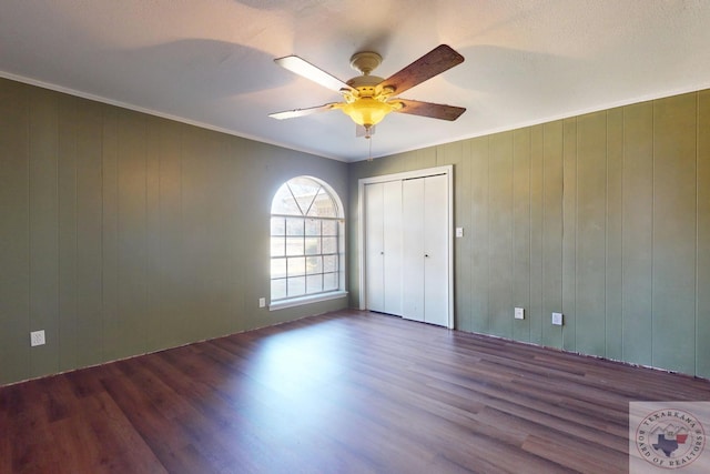 unfurnished bedroom featuring ceiling fan, dark wood-type flooring, and wooden walls