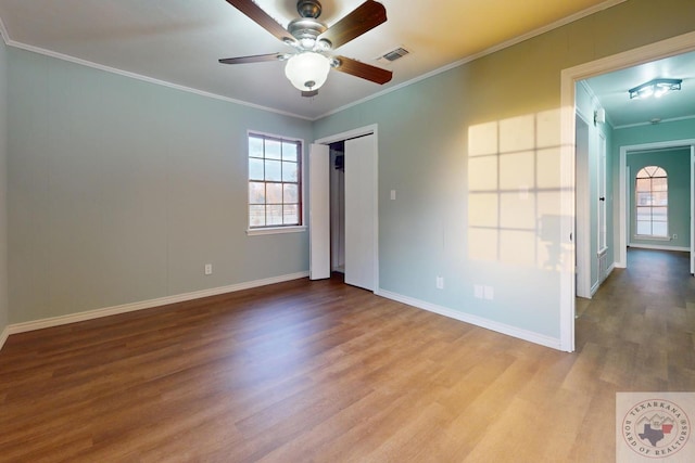 empty room with a healthy amount of sunlight, visible vents, wood finished floors, and ornamental molding