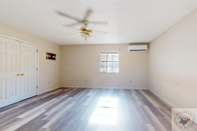 empty room with ceiling fan, light hardwood / wood-style floors, a textured ceiling, and a wall unit AC