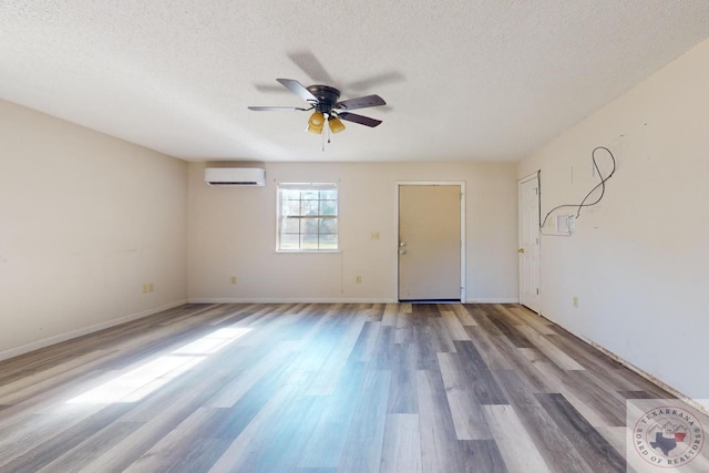 unfurnished room with ceiling fan, a textured ceiling, a wall unit AC, and light wood-type flooring