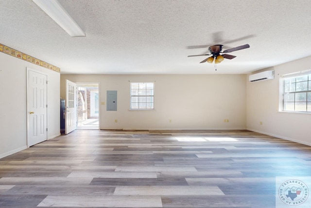 spare room featuring electric panel, hardwood / wood-style flooring, a wall unit AC, and a healthy amount of sunlight