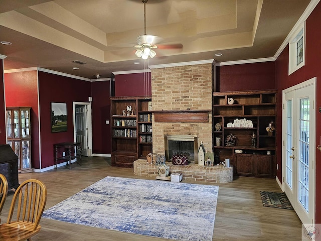 living room with crown molding, ceiling fan, a raised ceiling, a brick fireplace, and hardwood / wood-style floors