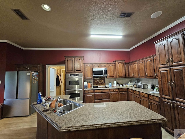 kitchen with appliances with stainless steel finishes, sink, light wood-type flooring, a center island with sink, and crown molding