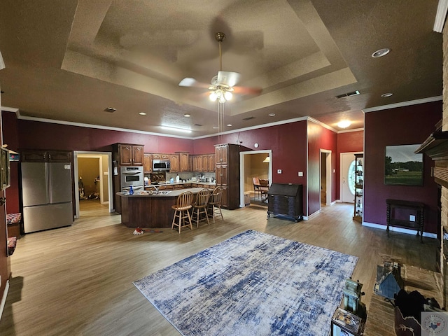 interior space with light hardwood / wood-style floors, appliances with stainless steel finishes, a kitchen breakfast bar, a kitchen island, and a tray ceiling