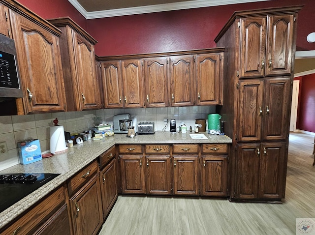 kitchen with light hardwood / wood-style flooring, black cooktop, tasteful backsplash, light stone counters, and ornamental molding