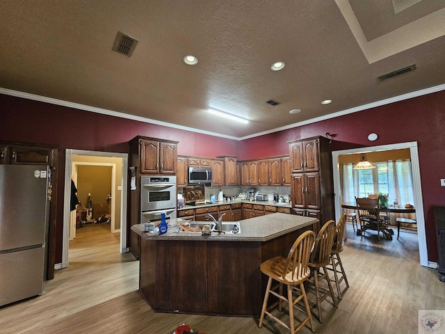 kitchen with appliances with stainless steel finishes, light hardwood / wood-style flooring, a kitchen bar, ornamental molding, and a center island with sink