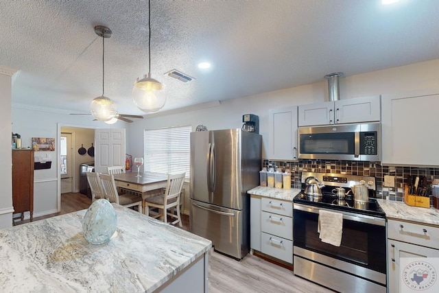 kitchen with appliances with stainless steel finishes, decorative light fixtures, white cabinets, light stone countertops, and decorative backsplash