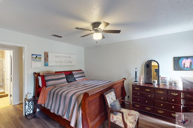 bedroom with ceiling fan, connected bathroom, hardwood / wood-style flooring, and a textured ceiling