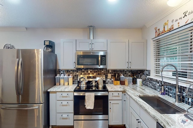 kitchen with light stone countertops, white cabinets, appliances with stainless steel finishes, decorative backsplash, and sink