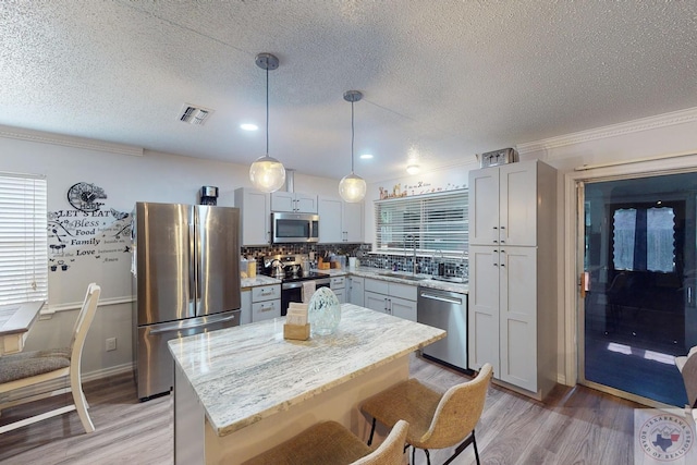 kitchen with pendant lighting, light wood-type flooring, a kitchen island, decorative backsplash, and stainless steel appliances