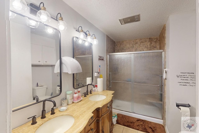 bathroom with a textured ceiling, tile patterned floors, a shower with door, vanity, and toilet