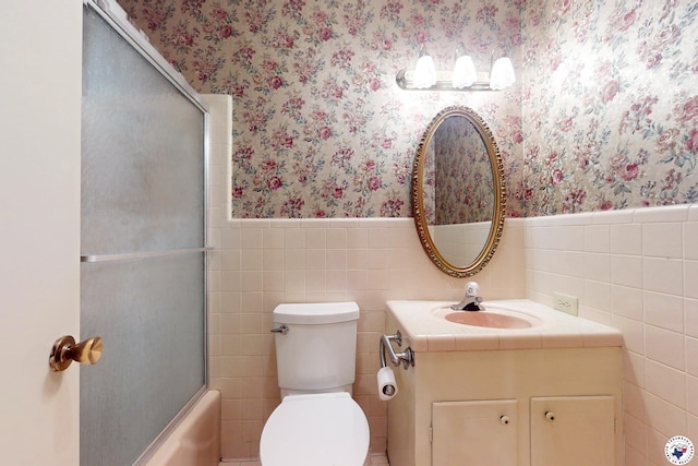 1315 Holloway Dr, Texarkana, TX 75503 - bathroom with wallpapered walls, vanity, wainscoting, tile walls, and combined bath / shower with glass door