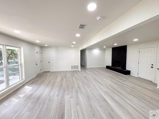 unfurnished living room with light wood-type flooring and a brick fireplace