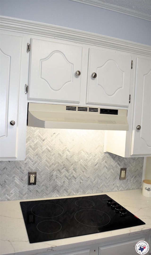 kitchen with light stone counters, decorative backsplash, black electric cooktop, white cabinets, and under cabinet range hood